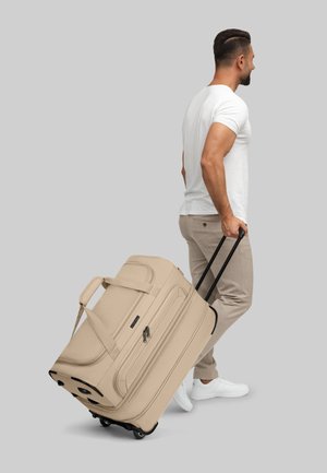 Borsa da viaggio beige con ruote, superficie texture, doppio manico e manico nero retrattile; ruote visibili alla base.