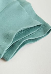 Tissu plié bleu sarcelle clair avec des coutures côtelées visibles et une texture lisse sur une surface claire unie.