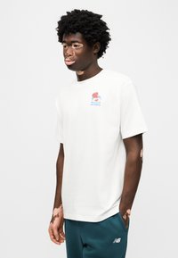 Λευκό βαμβακερό T-shirt με στρογγυλή λαιμόκοψη, με πολύχρωμο γραφικό σχέδιο στο αριστερό στήθος. Συνδυάζεται με σκούρο πράσινο παντελόνι φόρμας.