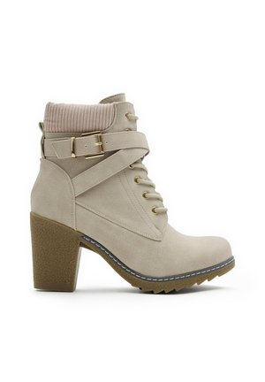 Botín beige con superficie texturizada, parte delantera con cordones, herrajes dorados y un cuello tipo calcetín acanalado. Presenta un tacón grueso y una suela con relieve.