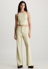 Világoszöld crop top, nyakkivágásos kialakítással; az alsó ruházatot illeszkedő, széles szárú nadrággal párosítva, amely függőleges varratokkal és hagyományos gombos záródással rendelkezik.