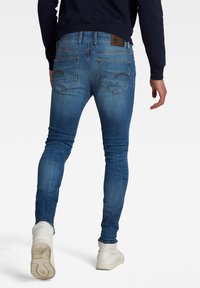 Slim blå jeans med en blekt textur, bakfickor med sydde detaljer och ett brunt logopatch vid midjan. Stylad med vita sneakers.