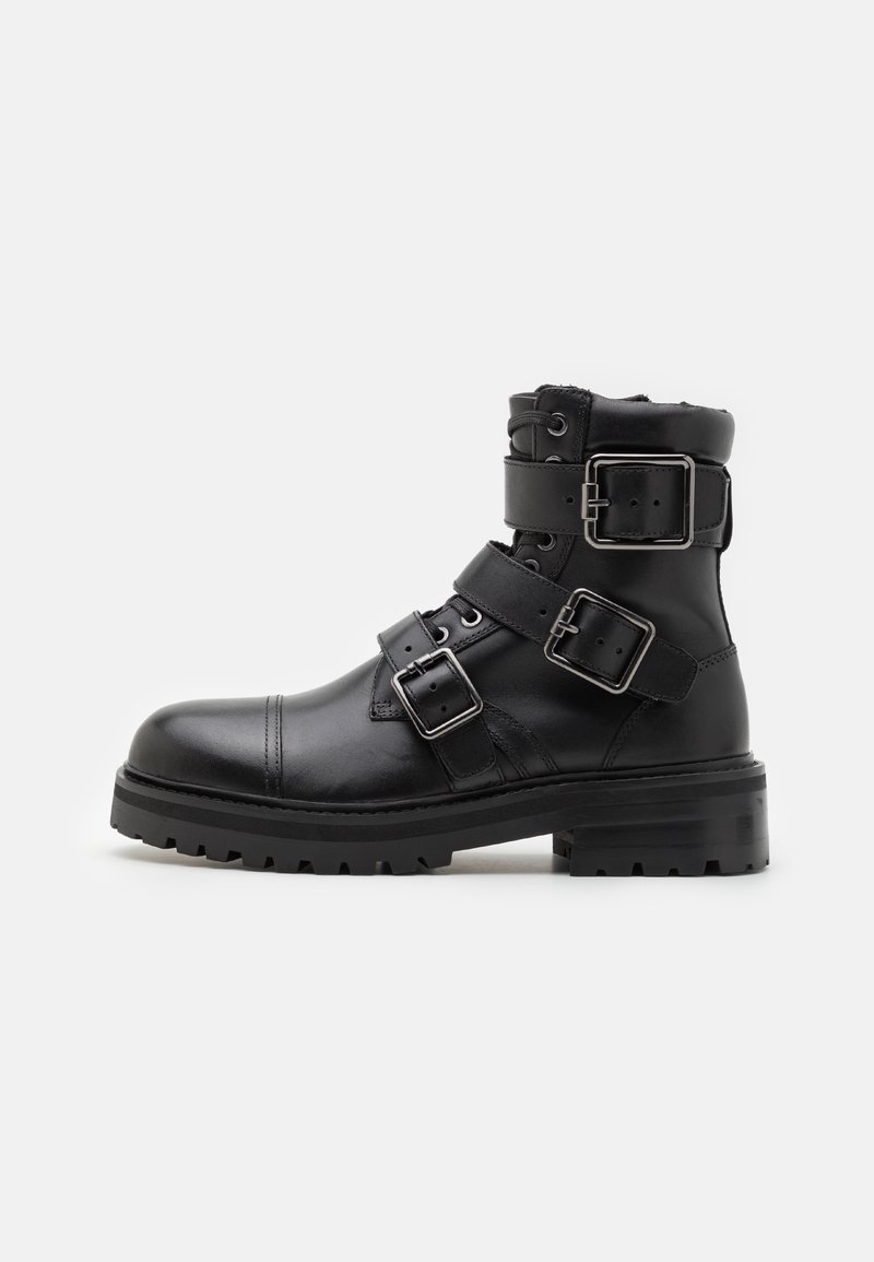 Bota de cuero negra hasta el tobillo con tres correas ajustables y hebillas plateadas. Presenta una punta redondeada y una suela de goma texturizada para mayor tracción.