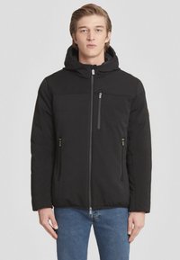 Giacca nera imbottita con cappuccio, dotata di tasca a zip sul petto, due tasche laterali e una texture liscia. Design semplice, vestibilità calda.