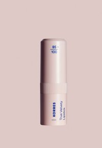 El lápiz labial True Velvety de Korres en un suave tubo rosa; presenta una sección acanalada, texto en azul y un diseño de tapa redondeada.