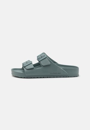 Slide sandal in muted teal, made of rubber with two adjustable buckled straps. Features a textured footbed and ridged outsole for grip.