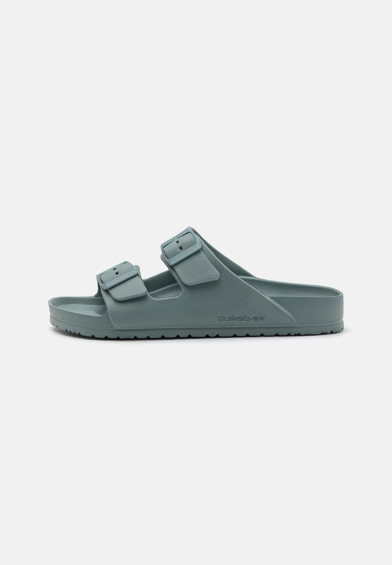 Kényelmes, tompa tengerzöld színű papucs, amely gumi anyagból készült, és két állítható csatos pánttal rendelkezik. Texturált talpbetét és bordázott talp jellemzi, ami biztosítja a tapadást.