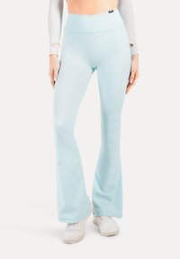 Pantalones de campana de tiro alto en azul claro, combinados con zapatillas blancas y una camiseta de manga larga con agujeros para los pulgares en las mangas.