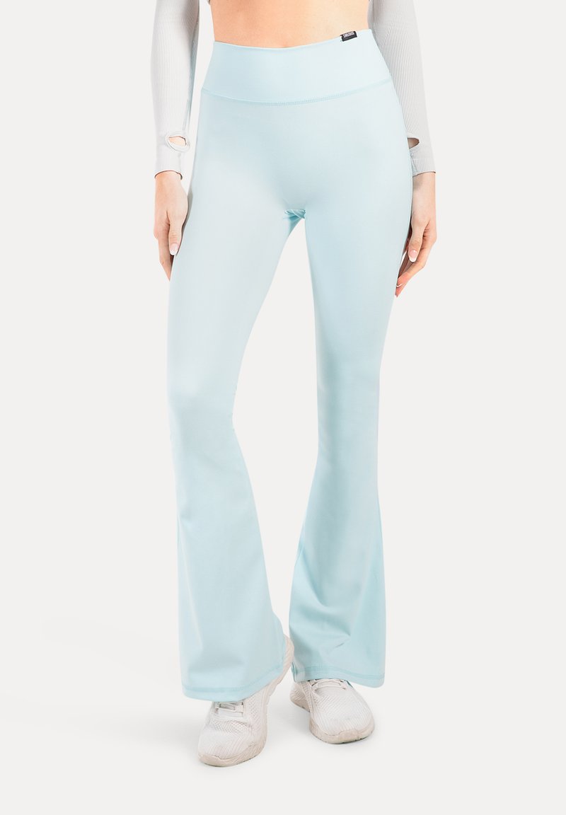 Pantalones de campana de tiro alto en azul claro, combinados con zapatillas blancas y una camiseta de manga larga con agujeros para los pulgares en las mangas.