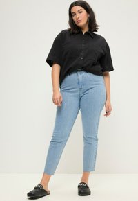 Camisa negra de manga corta con botones, combinada con jeans de tiro alto azul claro con rayas verticales. Usada con zapatos negros tipo slip-on.