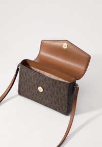 Hnědá crossbody taška se vzorem, se zlatým uzávěrem, béžovým koženým interiérem a dlouhým nastavitelným popruhem.