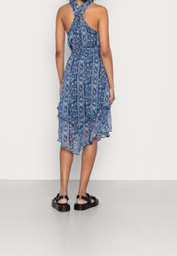 Blå blomsterklänning med halterneck, lager av volanger och en flytande design. Matchad med svarta sandaler.