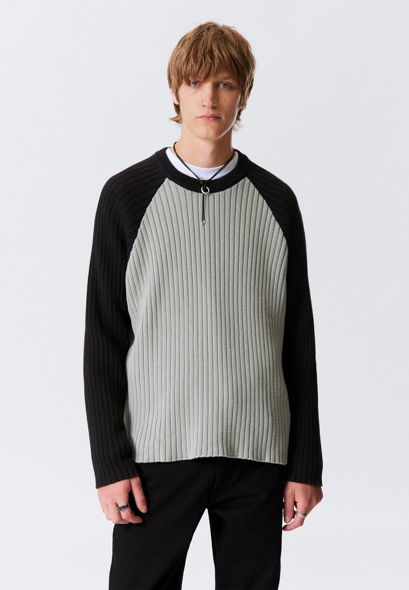 Ribbed sweater with a light gray front and black raglan sleeves. Features a round neck and a subtle texture, offering a relaxed fit.