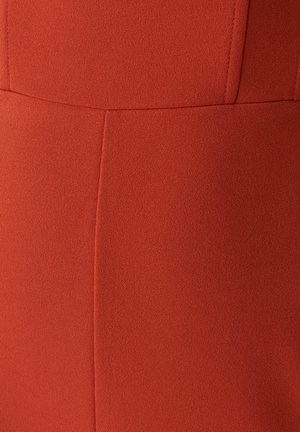 Close-up van roestkleurige textuurstof met zichtbare naden en stiksels.