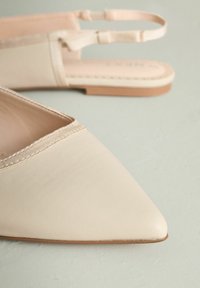 Chaussures slingback en cuir beige avec un bout pointu, des coutures texturées, une semelle marron clair, et une bride ajustable.