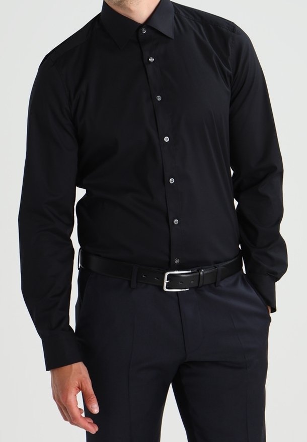 Camicia da uomo nera a maniche lunghe in tessuto satinato con colletto classico, bottoni frontali e vestibilità slim, abbinata a pantaloni scuri e una cintura.