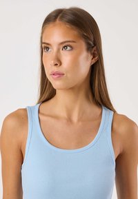 Vaaleansininen ribbineulottu hihaton toppi, jossa on pyöreä pääntie ja leveät olkaimet. Sileä pinta ja hienovaraiset saumat. Ei huomattavia kuvioita tai koristeita.