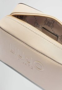 Lyserød tekstureret kosmetikpung med guld lynlås. Har det præget "LIU-JO" logo og et mønstret indvendigt foer. Lynlås lukning øverst.