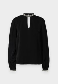 Blouse noire à manches longues avec un col haut dotée d'une ouverture en forme de gouttière, des poignets ornés et une texture lisse. Accentuée d'un col décoratif.