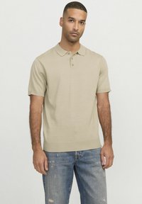 Polo en tricot beige à manches courtes, avec un col et une patte de boutonnage à trois boutons, associé à un jean bleu déchiré.
