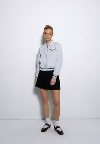 Szara rozpinana bluza z kołnierzykiem, ozdobiona trzema gwiazdkami; zestawiona z czarną plisowaną spódnicą i brązowymi butami oraz białymi skarpetkami.