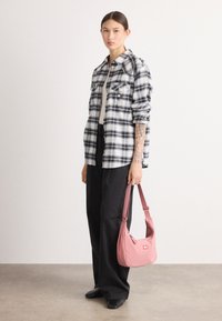 Bolso de tela rosa con forma curvada y correa corta, combinado con una camisa de cuadros en blanco y negro y pantalones anchos negros.