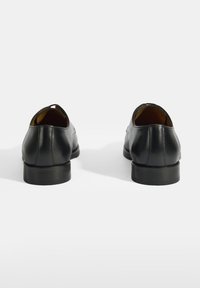 Chaussures en cuir noir avec une finition lisse, bout arrondi et talon bas. Design simple avec une légère courbure au talon et des détails de couture.