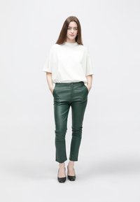 Valkoinen lyhythihainen t-paita yhdistetty istuviin vihreisiin nahkahousuihin, joissa on nappikiinnitys ja tyylikäs pinta, täydentäen mustilla avokkailla.