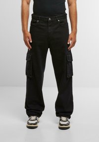 Črne cargo hlače se ponašajo z ohlapnim krojem, več stranskimi žepi in tradicionalnim petim žepnim dizajnom. Narejene so iz denim materiala z gladko teksturo.