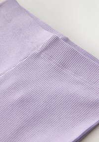 Svetlofialová rebrovaná látka s hladkou textúrou; obsahuje jemné švy a mierne elastický pás pre lepšie priliehanie.