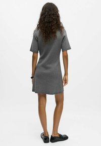 Robe grise à manches courtes avec une coupe décontractée, longueur mi-cuisse, fabriquée en tissu doux. Portée avec des chaussures noires à enfiler, présentant une texture unie.