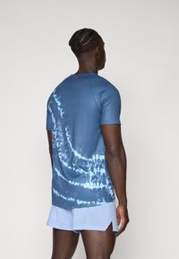 Blå tie-dye t-skjorte med korte ermer, med varierende nyanser og virvler, kombinert med lyseblå perforerte shorts. Myk tekstur.