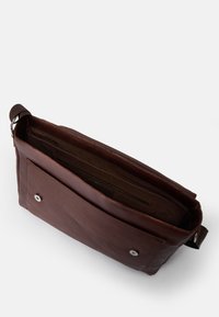 Brązowa skórzana torba na ramię o miękkiej teksturze, z przednią kieszenią, zatrzaskiem i materiałowym paskiem. Wnętrze ma wiele przegródek.