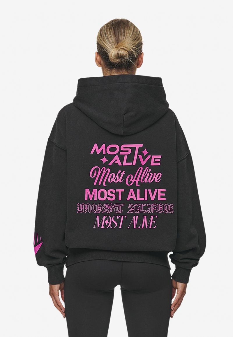 Černá mikina s kapucí, na které je vzadu výrazný růžový nápis "MOST ALIVE" napsaný různými fonty. Vyrobena z měkké látky, má klasickou kapuci a uvolněný střih.