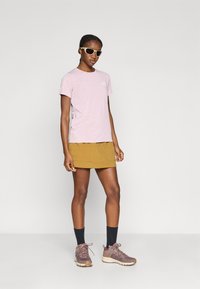 Ροζ ανοιχτόχρωμο κοντομάνικο T-shirt, κίτρινη φούστα, γκρι-καφέ παπούτσια πεζοπορίας, μαύρες κάλτσες μέχρι τον αστράγαλο και γυαλιά ηλίου. Καθημερινό ανοιχτόχρωμο σύνολο με τσέπες.