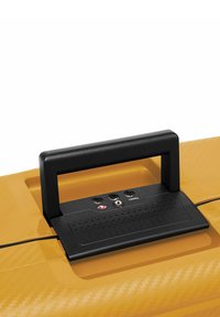 Valigia rigida gialla con manico in plastica nera e un pannello di controllo che presenta tre porte di ingresso e una superficie texturizzata.