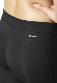 Czarne legginsy sportowe o gładkiej teksturze, przeszyciach oraz logo "climalite" umieszczonym na pasku w talii.