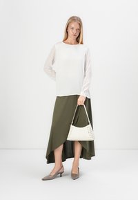 Weißes Langarmoberteil mit gestreiften Akzenten, asymmetrischer olivgrüner Rock, hellgraue High Heels und eine weiße Tasche mit Stoffdetails.