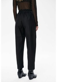 Zwarte, hoog-waist broeken met een relaxte pasvorm, voorzien van een gathered elastische tailleband en zijsplitten bij de enkels. Gepaard met haklaarzen.