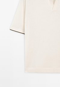 T-shirt a maniche corte, con scollo a V, in cotone beige chiaro con una consistenza liscia e bordature scure a contrasto sulle maniche. Design semplice e pulito.