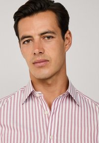 Pruhovaná košile na knoflíky se světle růžovými a bílými vertikálními pruhy, klasický límec a hladká textura látky. Obsahuje standardní knoflíky.