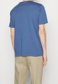 Blauw T-shirt met korte mouwen en een ronde hals, met een gladde textuur en nette stiksels. Draagt in combinatie met beige broek, wat een ontspannen pasvorm laat zien.