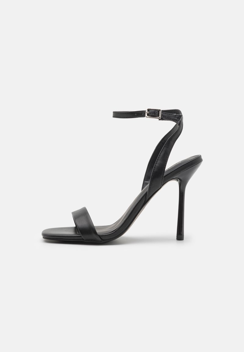 Sandale noire à talon haut avec fine bride à la cheville et boucle, bout ouvert et talon aiguille fin vue de côté sur fond uni.