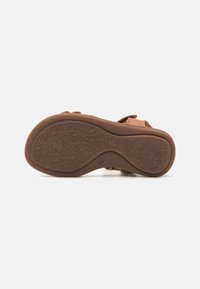 Tan sandaal met een gestructureerde rubberen zool met bloemmotieven. Verstelbare banden voor een veilige pasvorm. Zacht materiaal voor comfort.