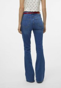 Ursnygga blå jeans med hög midja, som har två bakfickor och en subtil denimtextur. Ett rött bälte accentuerar midjan.