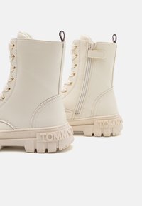 Crème leren enkellaarsjes met een chunky witte zool, gouden oogjes, zijrits en 'TOMMY' in de hak geperst.