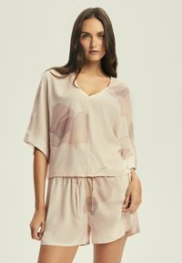 Jasnoróżowy zestaw odzieży domowej składający się z bluzki z krótkim rękawem w serek i luźnych szortów, ozdobiony delikatnymi wzorami kwiatowymi. Miękka struktura materiału.
