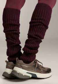 Adidași maro cu tălpi albe, asortați cu ciorapi de fleece burgundy cu textură ribbed. Materialul este texturat și elastic, se fixează confortabil.