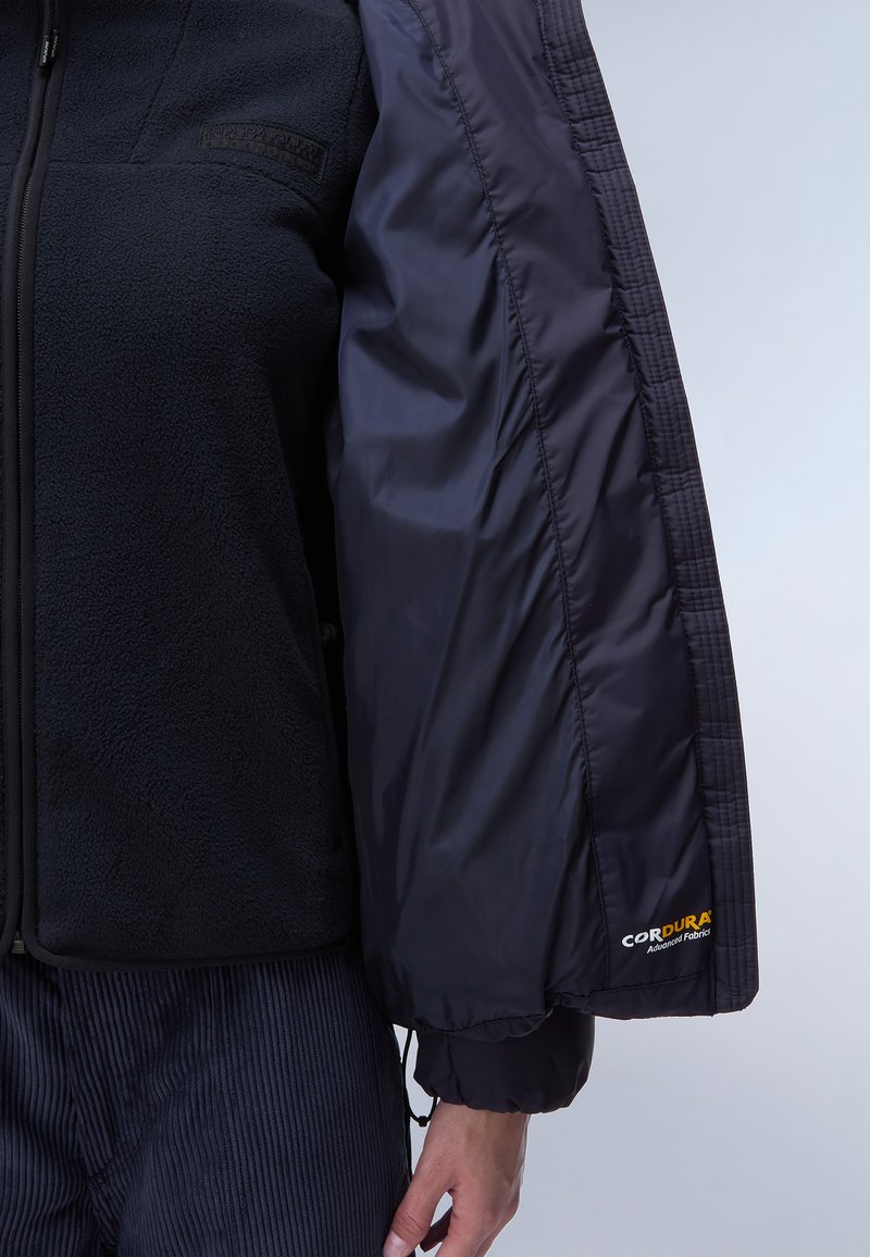 Czarna polarowa kurtka z gładkim czarnym rękawem z nylonu. Posiada logo Cordura na rękawie, regulowane mankiety oraz zamek błyskawiczny.