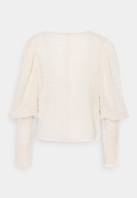 Vit texturerad topp med rund halsringning, puffärmar och långa åtsittande ärmar. Har ett subtilt rutmönster och en söm på baksidan.